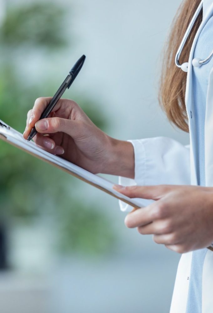 female-doctor-filling-up-medical-form-at-clipboard-while-standing-in-the-consultation--e1598498410893.jpg